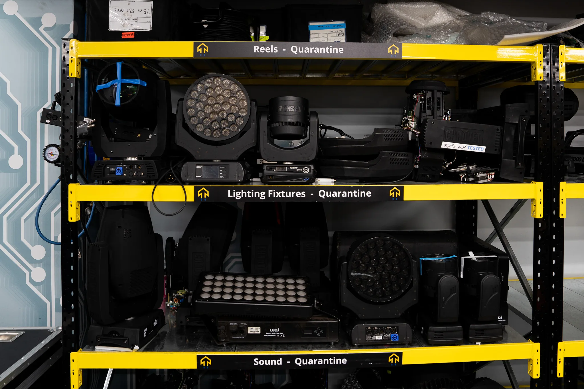 Moving head fixtures racked on labelled warehouse shelving for quarantine and testing
